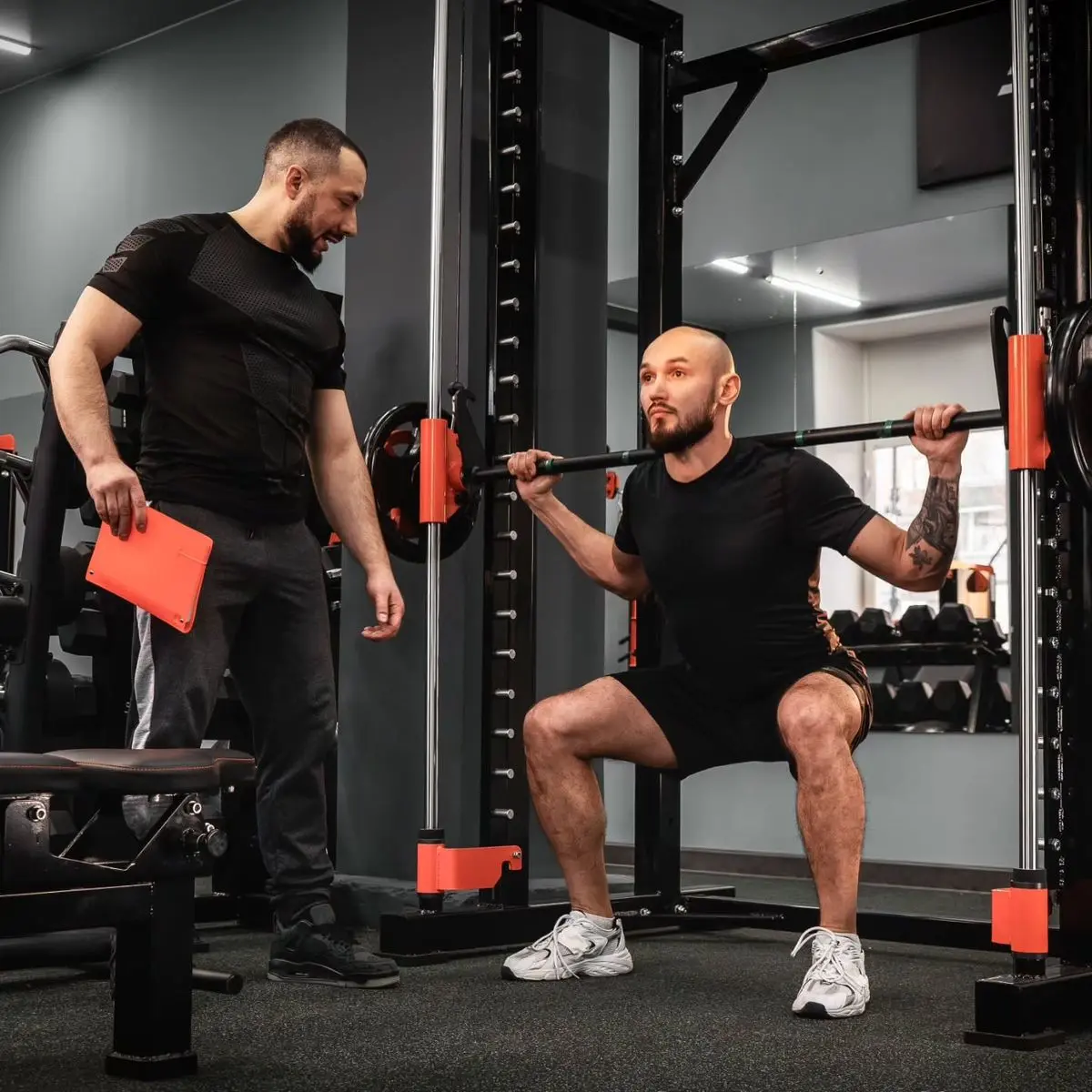 Personal trainer acompanhando um aluno no agachamento na academia